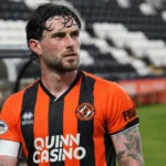 Will Ferry in het tenue van Dundee United langs de zijlijn van een voetbalveld.