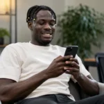 Promise David kijkt in een neutrale binnenruimte naar een smartphone.