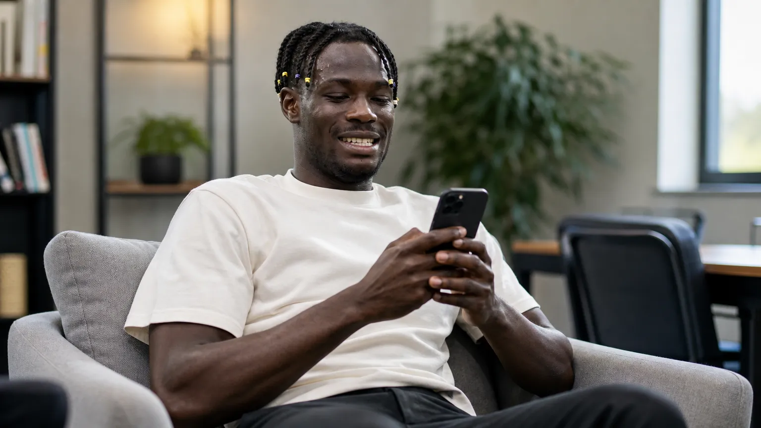 Promise David kijkt in een neutrale binnenruimte naar een smartphone.