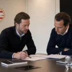 Twee clubmedewerkers bespreken documenten aan een tafel in een PSV-kantoor.
