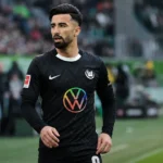 Mohamed Amoura staat geconcentreerd naast het veld in een donker Wolfsburg-tenue.