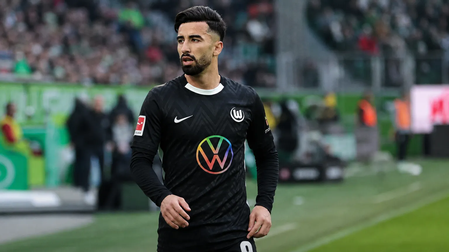 Mohamed Amoura staat geconcentreerd naast het veld in een donker Wolfsburg-tenue.