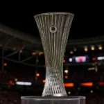 De Europa League-trofee staat centraal voor een wazige stadionachtergrond.