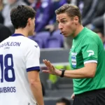 Een scheidsrechter in groen geeft aanwijzingen aan een speler tijdens een voetbalwedstrijd.