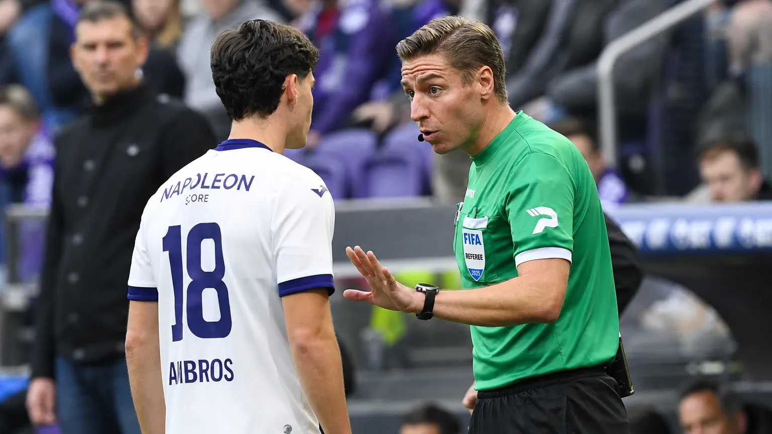 Een scheidsrechter in groen geeft aanwijzingen aan een speler tijdens een voetbalwedstrijd.