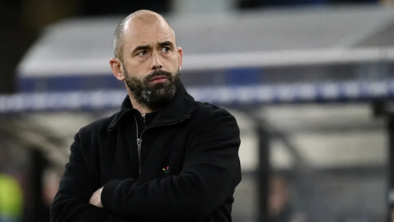 Een niet-spelende voetbalfiguur applaudisseert langs de zijlijn van een stadion.