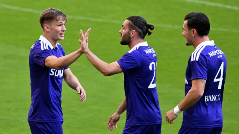 Drie voetballers in paarse wedstrijdkleding tijdens een gezamenlijke opwarming op het veld.