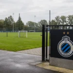 Leeg trainingsveld aan de jeugdopleiding van Club Brugge met het clubembleem aan de toegangspoort.