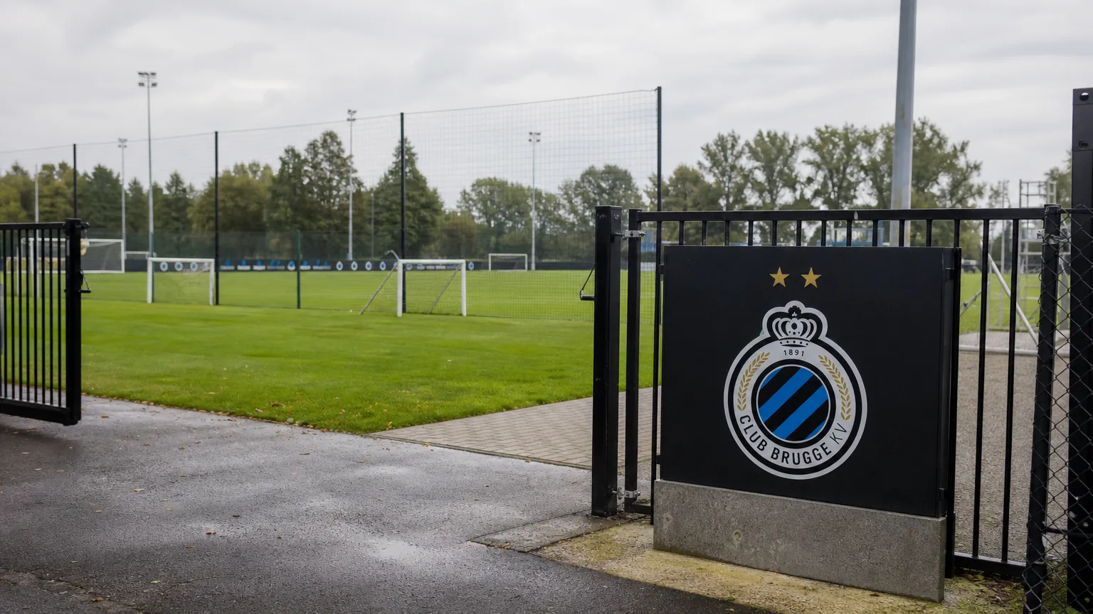 Leeg trainingsveld aan de jeugdopleiding van Club Brugge met het clubembleem aan de toegangspoort.
