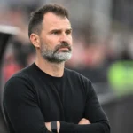 Een lid van de technische staf observeert rustig vanuit de technische zone van een stadion.