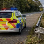 Een lege Engelse politiewagen naast een licht beschadigde vangrail langs de weg.