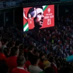 Supporters onder een groot herdenkingsscherm voor Diogo Jota in een stadion.