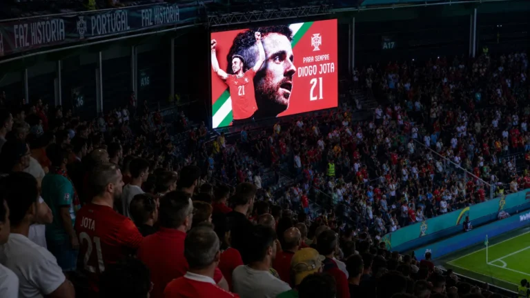 Supporters onder een groot herdenkingsscherm voor Diogo Jota in een stadion.