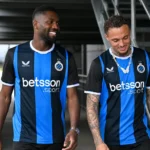 Twee voetballers in blauw-zwarte Club Brugge-tenues in een overdekte stadiongang.