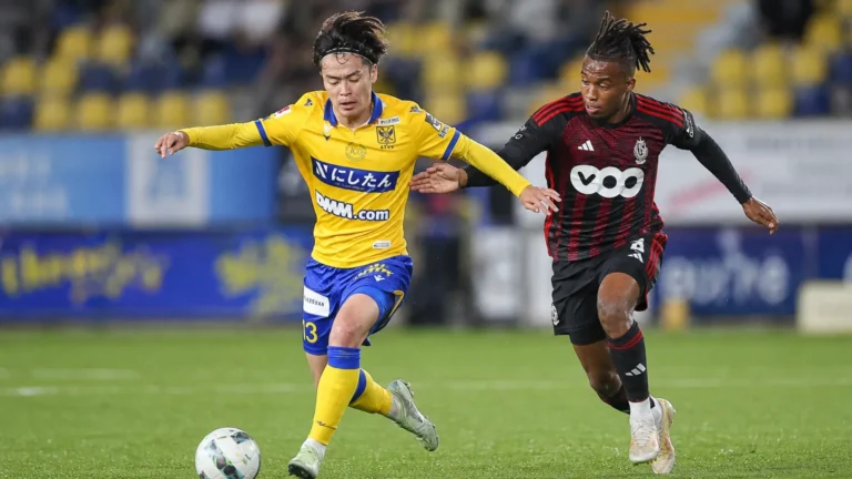 Twee voetballers in gele en zwart-rode wedstrijdtenues in een duel.