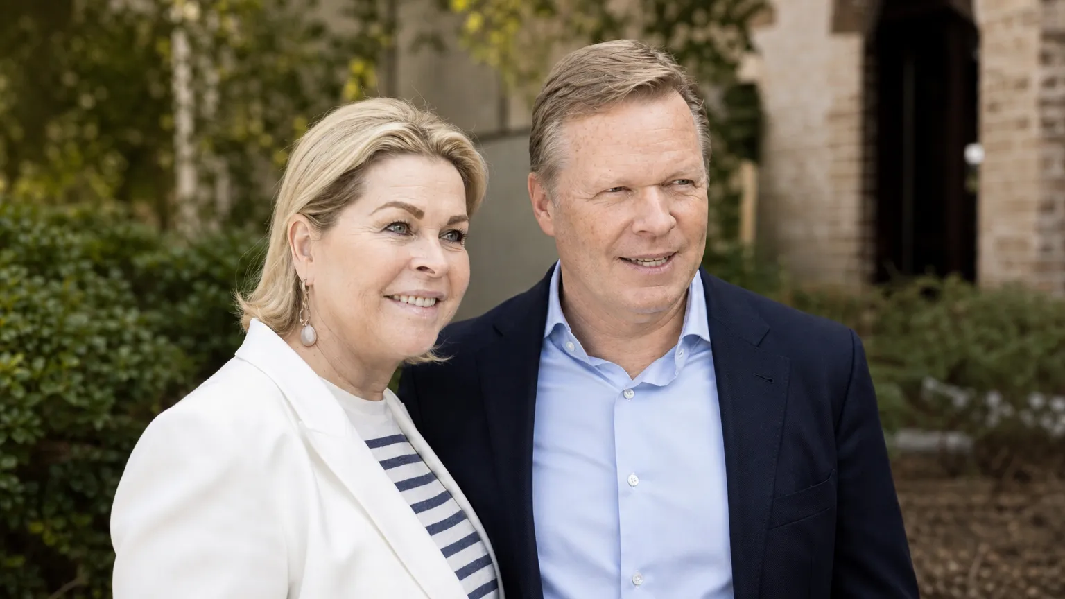 Een vrouw en man in nette kleding poseren samen op een rustige buitenlocatie.