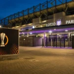 Verlichte ingang van het Lotto Park met een fysiek Europa League-wedstrijdbord.