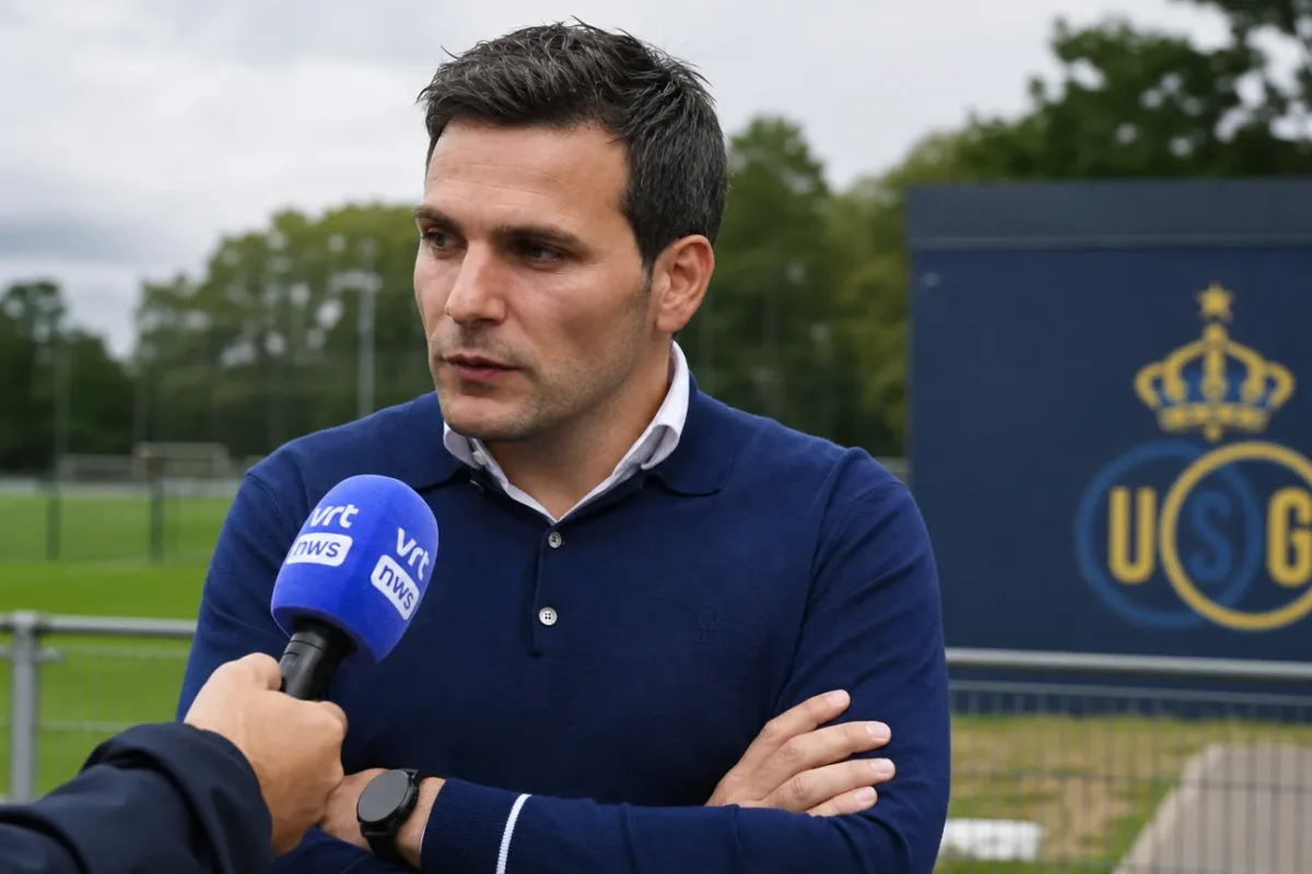 Een niet-spelende clubvertegenwoordiger wordt geïnterviewd naast een voetbalveld met een Union-embleem op een vast bord.