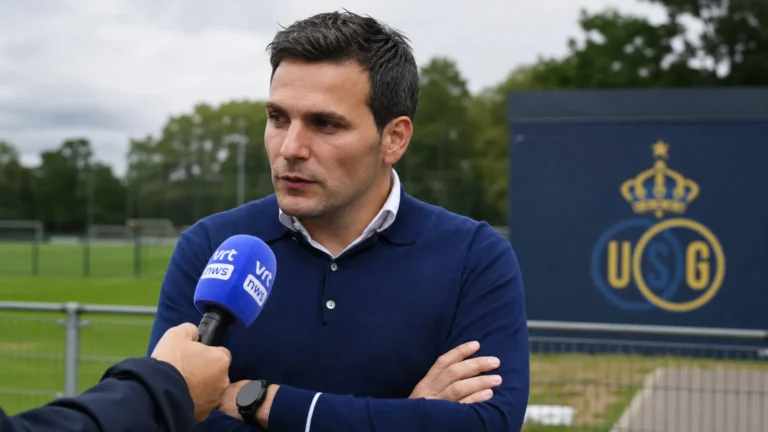 Een niet-spelende clubvertegenwoordiger wordt geïnterviewd naast een voetbalveld met een Union-embleem op een vast bord.