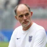 Thomas Tuchel in een wit Engeland-shirt tijdens een rustige terugblik in een stadionomgeving.