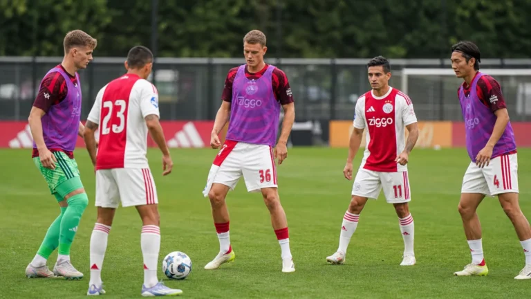 Een groep Ajax-spelers warmt op het trainingsveld op in rood-witte clubkleding.