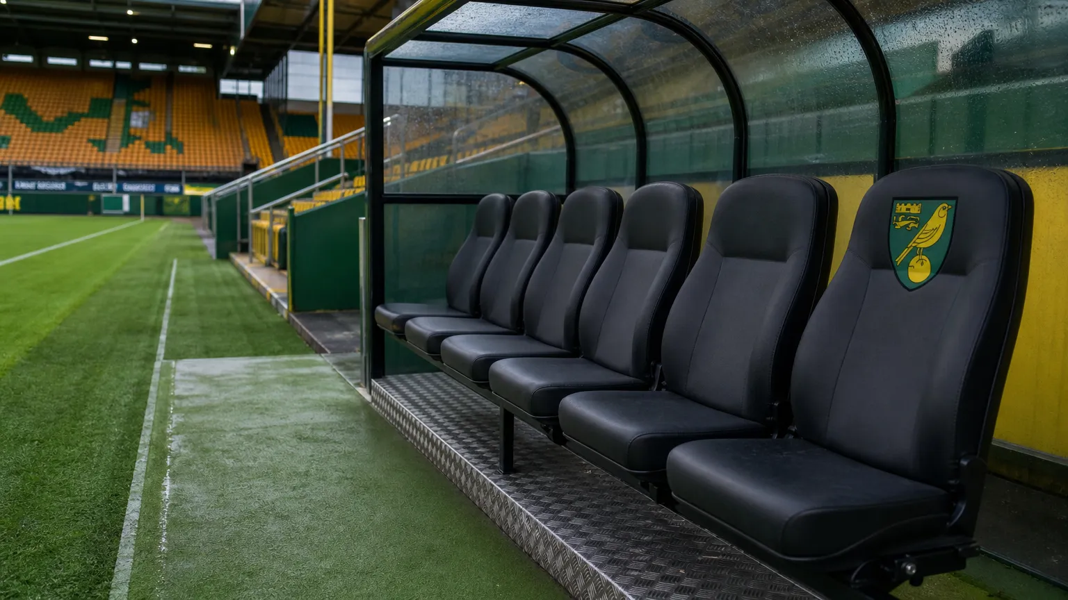 Een lege dug-out van Norwich City met een clubembleem op de vaste zitbank.