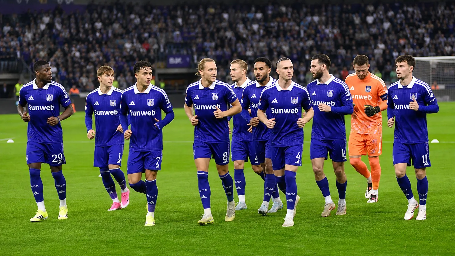 Anderlecht-spelers in paarse tenues tijdens een loopoefening op het veld.