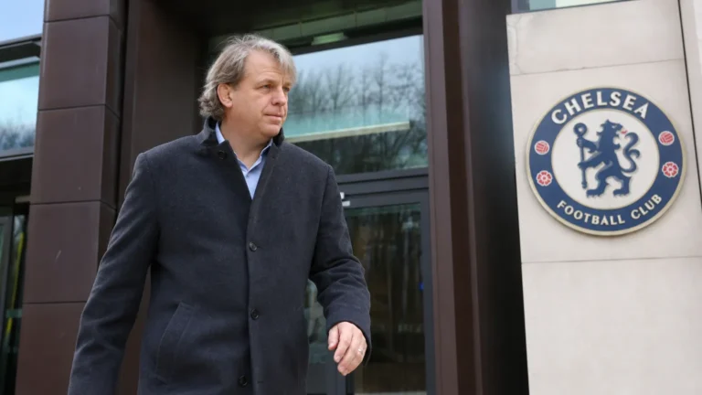 Todd Boehly in donkere jas bij de ingang van een Chelsea-clubgebouw.