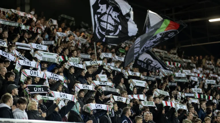Een groep OHL-supporters zwaait met sjaals en vlaggen in een volle tribune.
