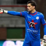 Louis Bostyn in blauw doelmanstenue van Zulte Waregem terwijl hij aanwijzingen geeft op het veld.