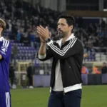 Een niet-spelende clubvertegenwoordiger en spelers in paarse tenues applaudisseren langs het veld.