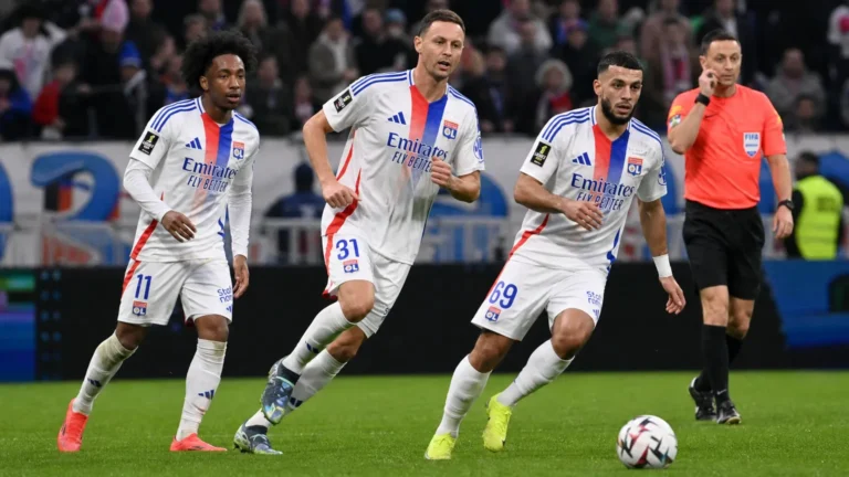 Drie spelers van Olympique Lyon tijdens een wedstrijdmoment met een scheidsrechter.