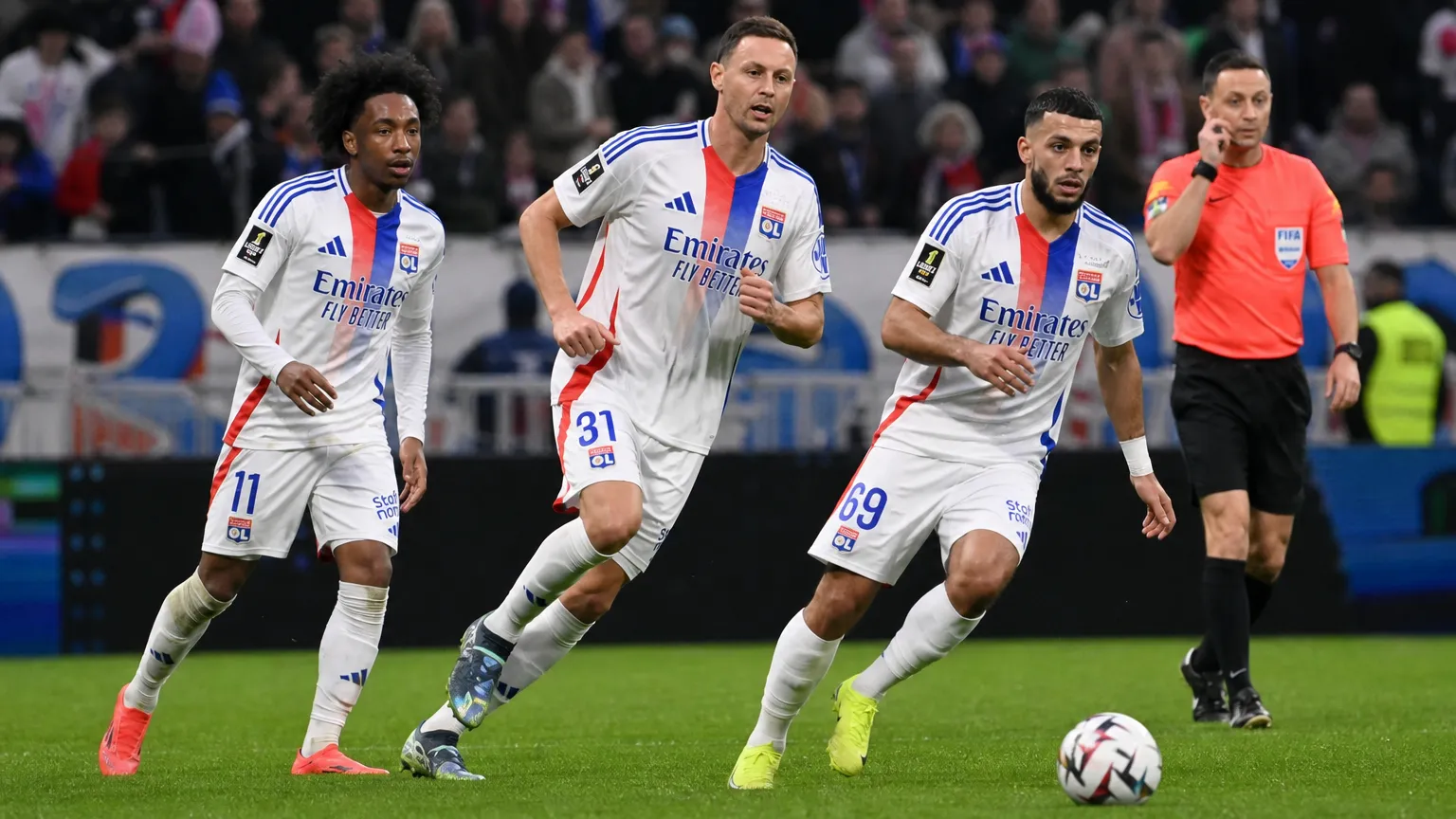 Drie spelers van Olympique Lyon tijdens een wedstrijdmoment met een scheidsrechter.