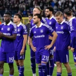 Een groep paars geklede voetballers verzamelt zich na de wedstrijd op het veld.