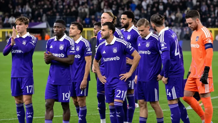 Een groep paars geklede voetballers verzamelt zich na de wedstrijd op het veld.