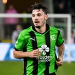 Gary Magnée in een groen-zwart shirt op de rand van een voetbalveld.