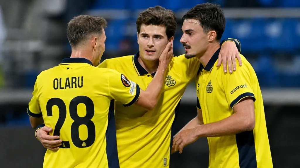 union-reeks-europa-schoofs-brede-selectie Drie voetballers in gele wedstrijdshirts vieren samen op het veld.