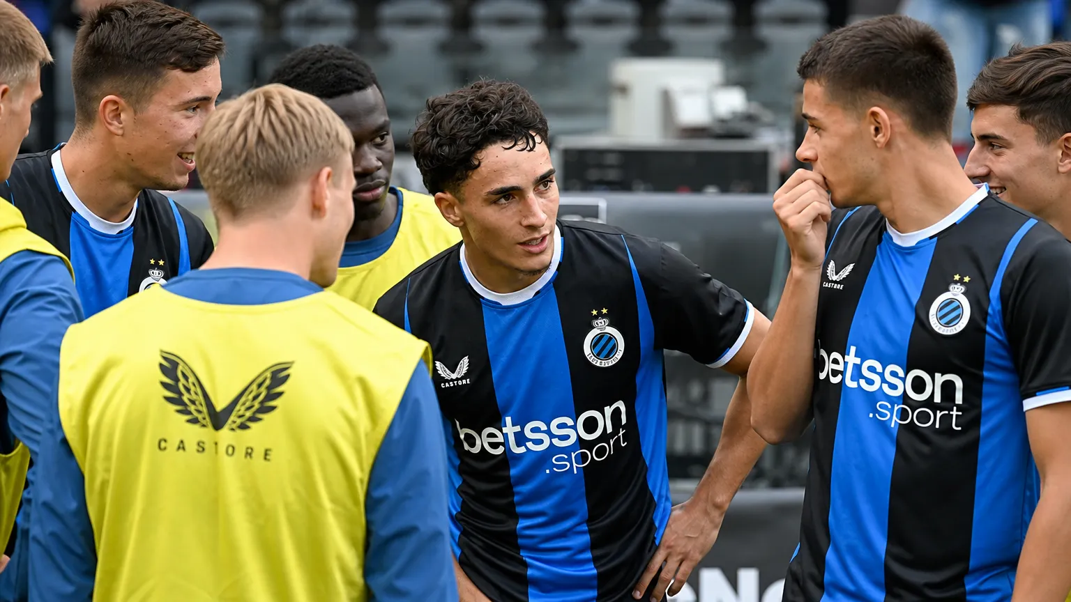 Een groep Club Brugge-spelers in blauw-zwarte wedstrijdkledij naast het veld.