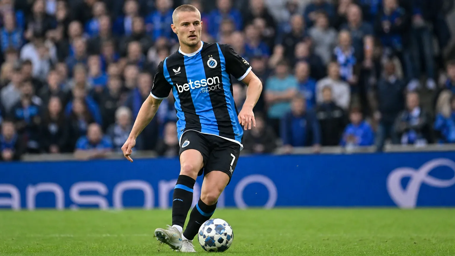 Een Club Brugge-speler in een blauw-zwart gestreept shirt tijdens een wedstrijd.