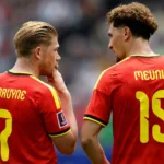 Twee spelers van de Belgische nationale ploeg overleggen op het veld in rode tenues.