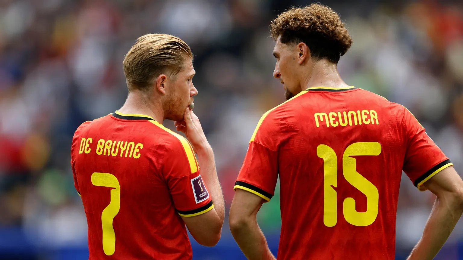 Twee spelers van de Belgische nationale ploeg overleggen op het veld in rode tenues.