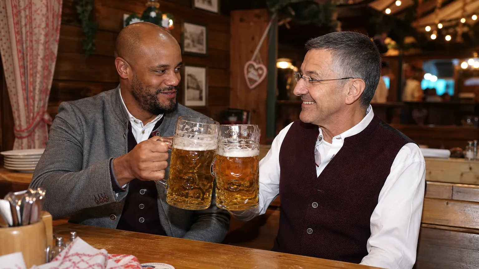 Twee bezoekers in traditionele Beierse kleding heffen bierpullen in een Oktoberfestzaal.