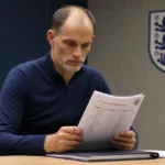Een Engelse bondscoach bekijkt een selectiedossier in een officiële mediaruimte.