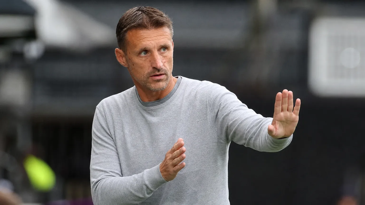 Een OH Leuven-coach in een grijze trui gebaart vanuit de technische zone.