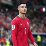 Cristiano Ronaldo in het rode tenue van Portugal aan de zijlijn van een stadion.