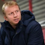 Sven Vandenbroeck zit in een stadionomgeving en kijkt aandachtig opzij.