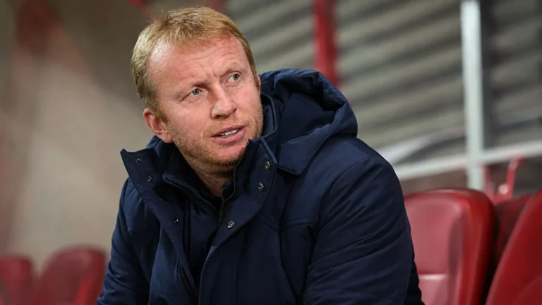 Sven Vandenbroeck zit in een stadionomgeving en kijkt aandachtig opzij.