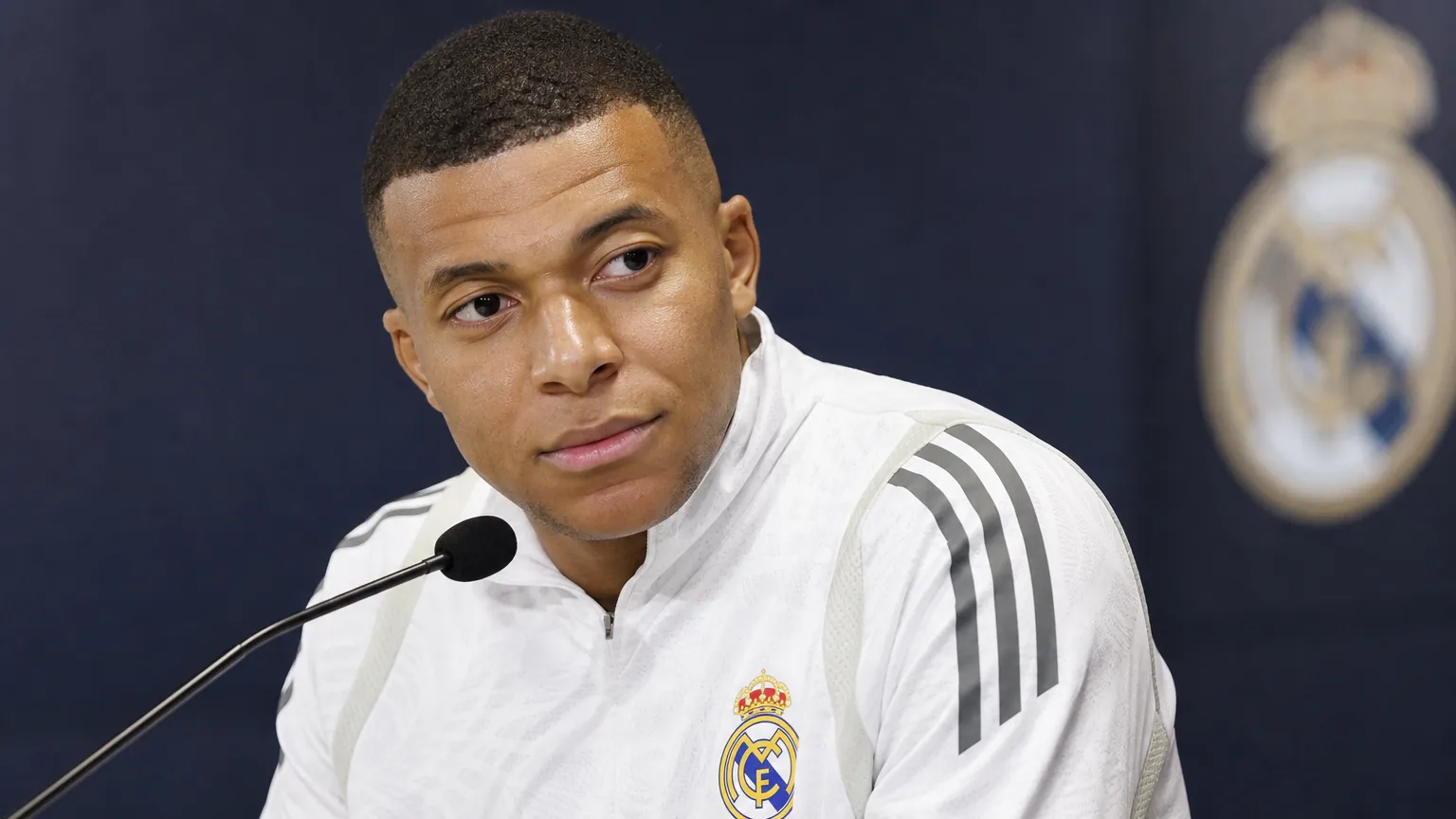 Kylian Mbappé zit tijdens een media-interview achter een microfoon in Real Madrid-kleding.