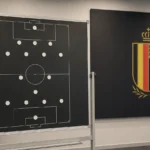 Een leeg selectiebord in de briefingruimte van de KBVB met het bondslogo op een wandpaneel.