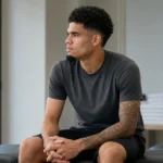 Luis Díaz rust in neutrale sportkleding in een rustige binnenruimte.